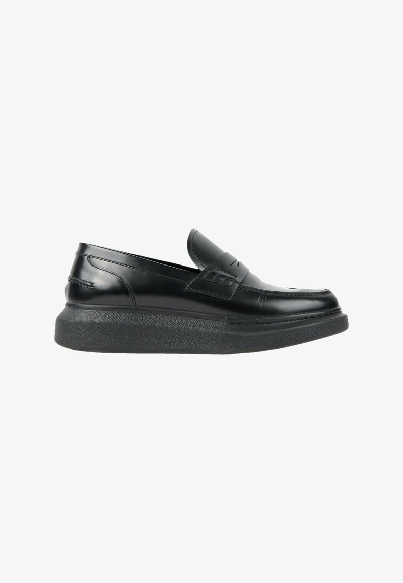 Mocassin en cuir noir avec une semelle épaisse texturée et un détail de bride décorative sur le dessus, vue de côté sur fond blanc.