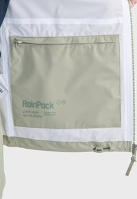 Lichtgewicht regenjack in groen en wit, met een ritszak, ademend materiaal en tekstbranding op de opbergzak.