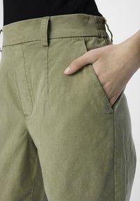 Pantalons kaki avec une texture lisse, dotés d'une taille haute avec un élastique froncé et de poches latérales.
