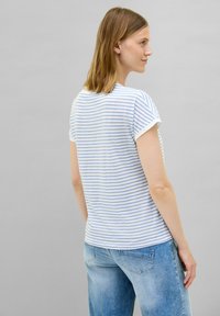 Stribet kortærmet T-shirt i hvid og lys blå, lavet af bomuld. Har rund hals og opkrøllede ærmer. Kombineret med lys blå jeans.