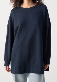 Sudadera de manga larga de color azul marino con cuello redondo, corte relajado y puños acanalados. Textura suave, con dobladillo cosido y aberturas laterales.