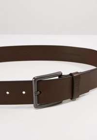 Bruine leren riem met een vierkante, metalen gesp. Heeft een gladde textuur, meerdere gaten voor maatverstelling en reliëfbranding.
