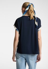 Top blu navy a maniche corte con accenti in seta a fantasia sulle maniche, scollatura rotonda e vestibilità comoda; abbinato a jeans blu chiaro.