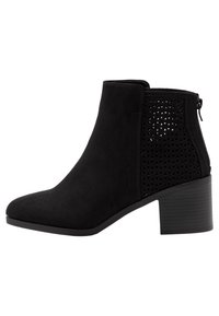 Stivale alla caviglia in suede nero con un design a taglio geometrico sul lato, caratterizzato da un tacco alto e una zip laterale per facilitare l'indossamento.