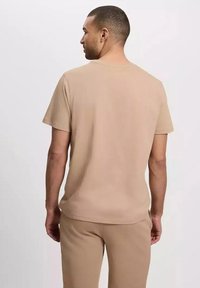Beżowa koszulka z krótkim rękawem, wykonana z miękkiej bawełny. Posiada klasyczny okrągły dekolt i luźny krój, bez widocznych logo czy wzorów.