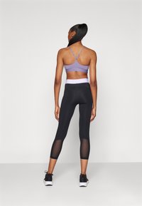 Paarse sportbeha met verstelbare bandjes, gecombineerd met zwarte leggings met een mesh paneel en een contrasterende tailleband.