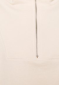 Sudadera de color crema con cremallera frontal, textura acanalada y diseño de costura plana cerca del cuello.