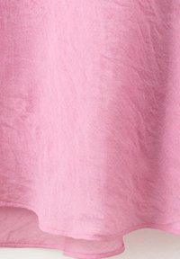 Tissu de rideau transparent rose doux avec de subtiles rides et un ourlet cousu au bord inférieur.