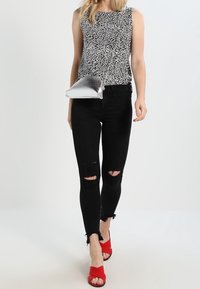 Svart och vit mönstrad ärmlös topp, svarta rivna skinny jeans, röda öppna sandaler och en glänsande silverfärgad kuvertväska.