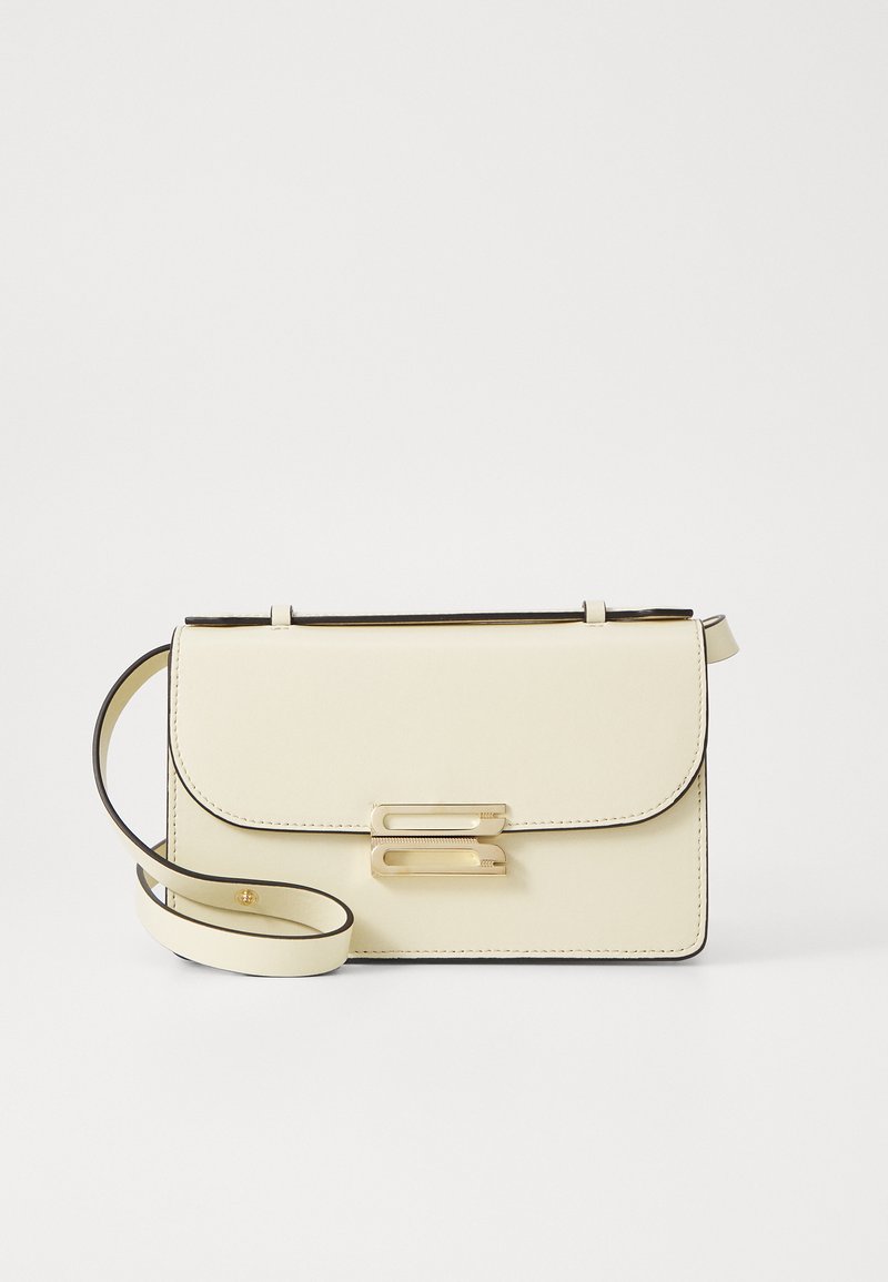 Bolsa crossbody em couro creme com fecho de aba, acessórios em tom de ouro, alça ajustável e bordas pretas em contraste.