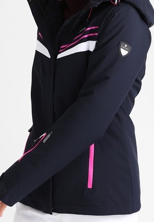Woman wearing black jacket with pink and white stripes, pink zipper accents, and a logo patch on the upper sleeve.