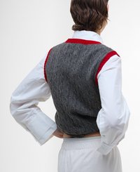 Gilet en maille torsadée gris avec un col côtelé rouge, porté par-dessus une chemise blanche à manches longues. Présente un design court et un tissu texturé.