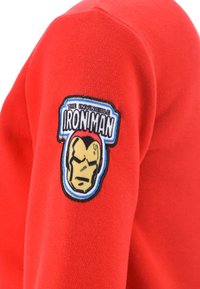 Red fabric with a patch showing Iron Man's helmet and the text "The Invincible Iron Man" on the upper arm area of a garment.