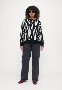 Μαύρο και άσπρο ριγέ πουλόβερ από μαλακή πλέξη, συνδυασμένο με σκούρα φαρδιά τζιν και κόκκινα παπούτσια. Τα αξεσουάρ περιλαμβάνουν στενές μαύρες ηλιόλουστες γυαλιά.