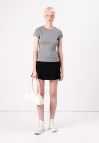 Top fitted grigio a maniche corte, gonna nera a campana, borsa bianca e sneakers alte bianche. Texture lisce, design semplice.