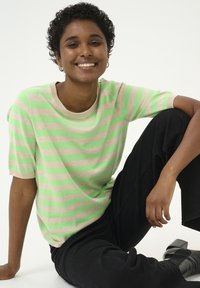 Short-sleeve sweater with green and beige stripes, round neckline, soft texture, paired with black pants and heeled shoes.