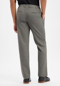 Grau gemusterte Hose mit geradem Schnitt, zwei Gesäßtaschen und Gürtelschlaufen, kombiniert mit schwarzen Schuhen.