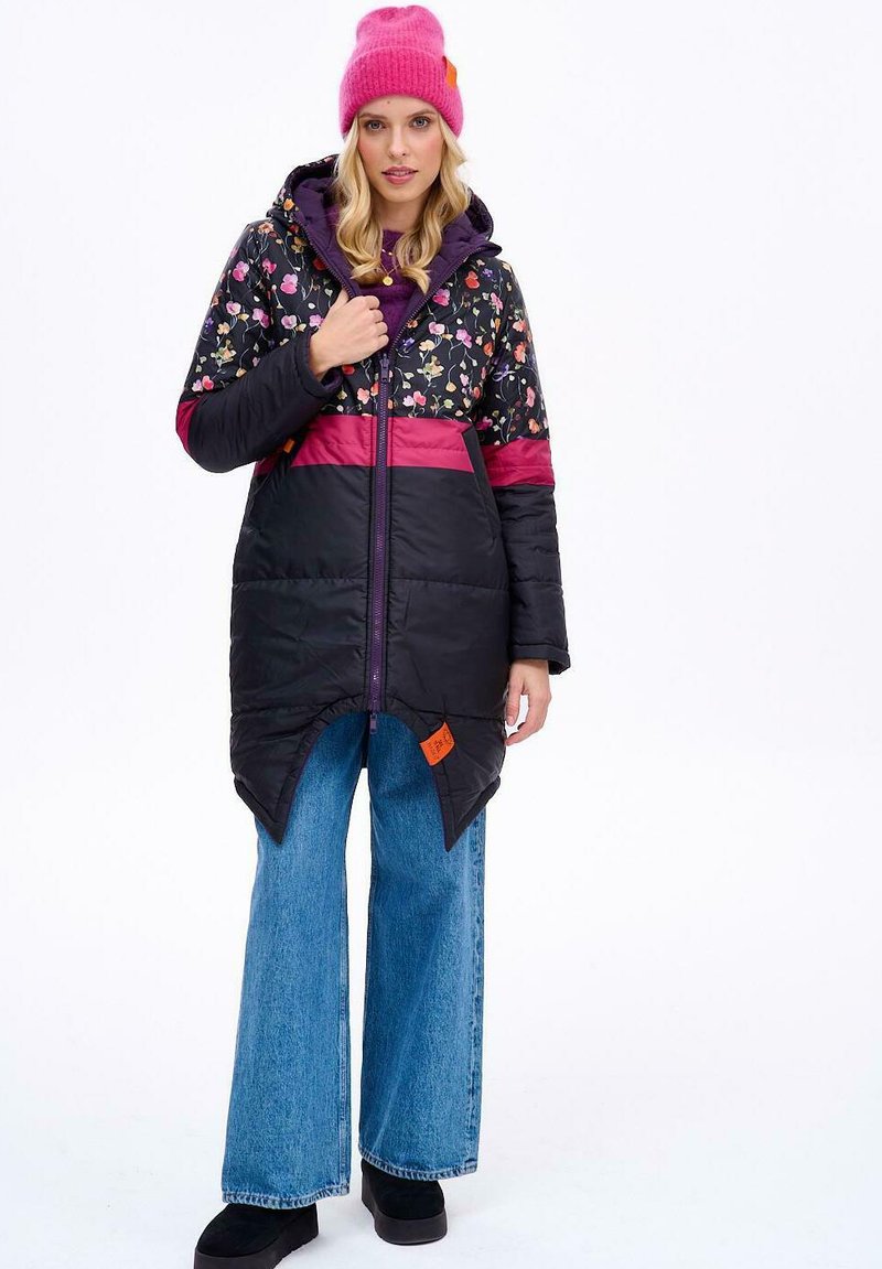 Zateplený černý zimní kabát s květinovým potiskem, růžovými a fialovými akcenty, předním zipem a unikátním špičatým lemem. Kombinovaný s širokými denimovými kalhotami.