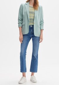 Mint green blazer, textured light sweater, blue straight-leg jeans, and white sneakers. Blazer features a single button and pockets.