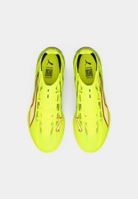 Helle gelbe Sportschuhe mit einer strukturierten Oberfläche, Schnürsenkeln und einem weißen Puma-Logo an der Seite. Modernes Design mit einer stromlinienförmigen Form.