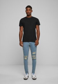 Fekete pamut póló, testhezálló dizájnnal, világoskék, kopott slim fit farmerrel, amelyen szakadás részletek találhatók, fekete-fehér tornacipővel viselve.