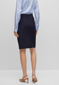 Jupe crayon bleu marine au design ajusté, fermeture éclair au dos et tissu lisse. Associée à un chemisier en satin bleu clair à manches longues.