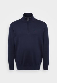 Pull-over à manches longues bleu marine avec une fermeture éclair d'un quart et un petit logo rouge, blanc et bleu sur la poitrine gauche.
