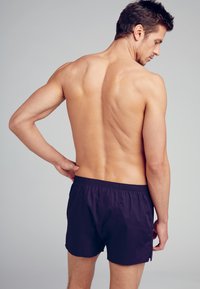 Pantaloni da bagno navy con elastico in vita, realizzati in tessuto leggero, con un taglio classico e una texture liscia, mostrati da dietro.