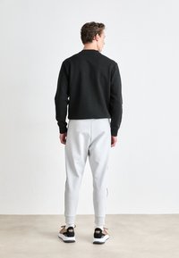 Black sweatshirt, relaxed fit, crew neckline, paired with light gray joggers, elastic cuffs, black side stripes, and neutral-tone sneakers.