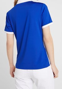 Niebieska koszulka polo z krótkim rękawem, z białym kołnierzykiem i akcentami na rękawach, wykonana z gładkiego materiału, charakteryzująca się dopasowanym krojem i czystymi liniami.