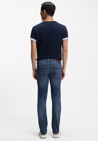 Námornícky modré tričko s krátkym rukávom a bielym lemom, skombinované s úzkymi modrými džínami a svetlými topánkami. Minimalistický a moderný dizajn.