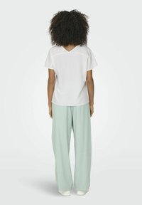 Haut blanc à manches courtes avec un dos en V, associé à un pantalon large en vert menthe clair. Le tissu semble lisse, avec une coupe décontractée et des détails de contraste subtils.