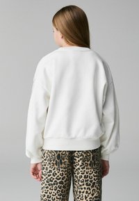 Vit sweatshirt med avslappnad passform, ribbade ärmslut och nederkant, tillsammans med mönstrade byxor i leopardtryck. Mjuk textur, oversized design.