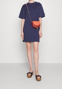 Námořnické bavlněné šaty ve stylu trička s volány na ramenou, doplněné červenou a burgundskou kabelkou přes rameno a černými platformovými sandály.