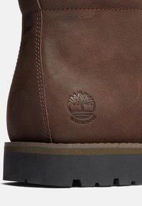 Stivale in pelle marrone con logo impermeabile, suola resistente, cuciture visibili e una texture liscia. Presenta un design solido e monocolore.