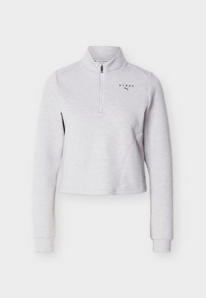 Dugotrajna svijetlosiva majica s četvrtastim patentnim zatvaračem i visokim ovratnikom s logotipima "HYROX" i Puma na lijevoj strani prsa.