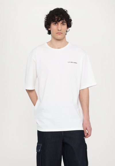 T-shirt en coton blanc avec un col rond et des manches courtes. Présente un texte noir subtil "LES BENJAMINS" sur la poitrine gauche.