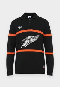 Črna polo majica z dolgimi rokavi in oranžnimi črtami, ki ima bel motiv pravega orla in tri gumbe na zapenjanju. Vključen vezeni logotip na prsih.