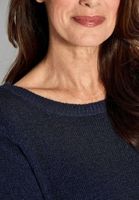 Navyblauer strukturierter Strickpullover mit rundem Ausschnitt. Nahaufnahme, die das Schulterdetail und die glatte Haut zeigt und das Gewebe des Kleidungsstücks hervorhebt.