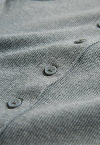 Gros plan sur un tissu côtelé gris avec quatre boutons gris cousus en ligne, montrant les détails de la texture et des coutures.