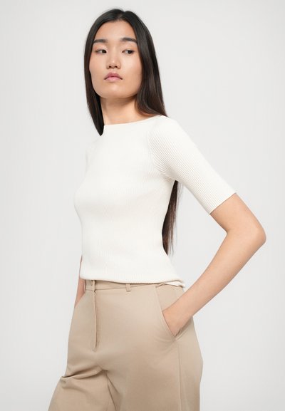 Top a maniche corte a coste di colore bianco sporco, con scollatura rotonda. Abbinato a pantaloni beigi a vita alta. Design semplice e aderente.