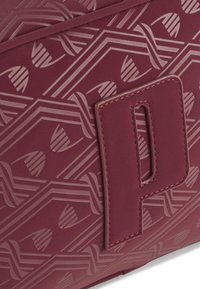 Burgundy väska med präglat geometriskt mönster, slät textur med en framträdande 'P' logopatch och sydda detaljer längs kanterna.