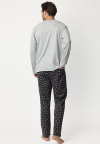 Suéter de algodón gris de manga larga y pantalones de pijama negros con un patrón colorido de pequeños iconos. Textura suave, corte relajado.