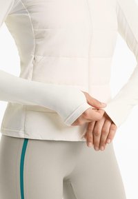 Doudoune blanche avec une texture lisse et une fermeture éclair sur le devant, associée à des leggings gris clair ajustés avec des rayures latérales turquoise.