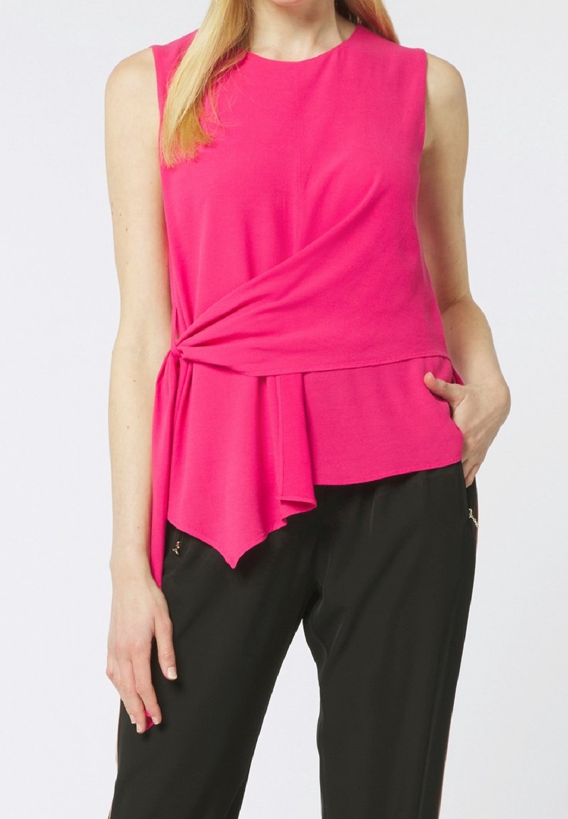 Haut rose sans manches avec un détail torsadé à la taille, présentant un décolleté arrondi et un ourlet fluide et asymétrique.