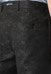 Black patterned trousers with a subtle floral design, featuring a flat front, side pockets, and a single buttoned back pocket.