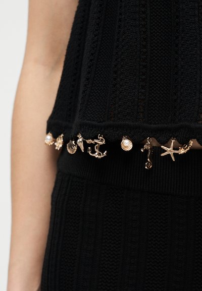 Μαύρο πλεκτό τοπ και φούστα με χρυσά ναυτικά διακοσμητικά, όπως άγκυρες, αστερίες, κοχύλια και ιππόκαμποι κατά μήκος της τελικής ραφής.