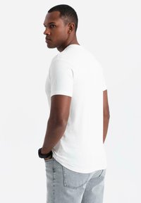 Bílý tričko s krátkým rukávem vyrobené z měkké látky, s klasickým kulatým výstřihem a hladkým, přiléhavým designem. Nosené s šedými džíny.
