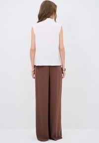 Witte mouwloze blouse met een kraag, gecombineerd met brede bruine trousers. De stof lijkt soepel en lichtgewicht, zonder zichtbare patronen.