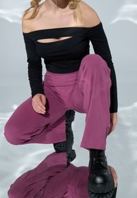 Haut noir décolleté avec détail découpé, associé à un pantalon côtelé taille haute magenta et des bottes noires épaisses à lacets.